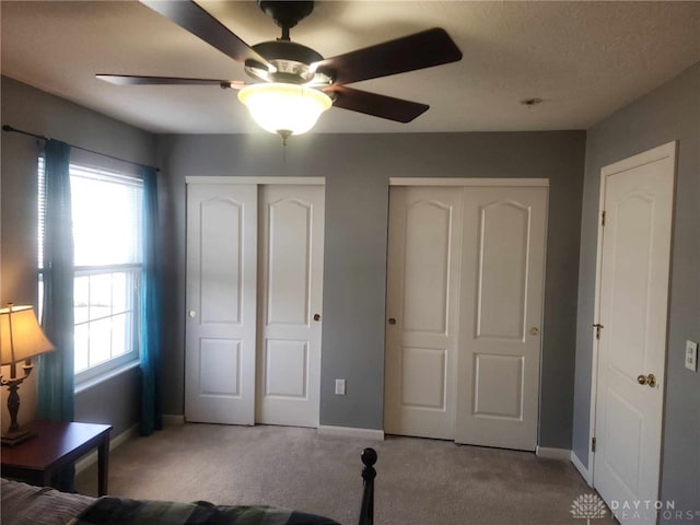 unfurnished bedroom with light carpet, ceiling fan, and multiple closets