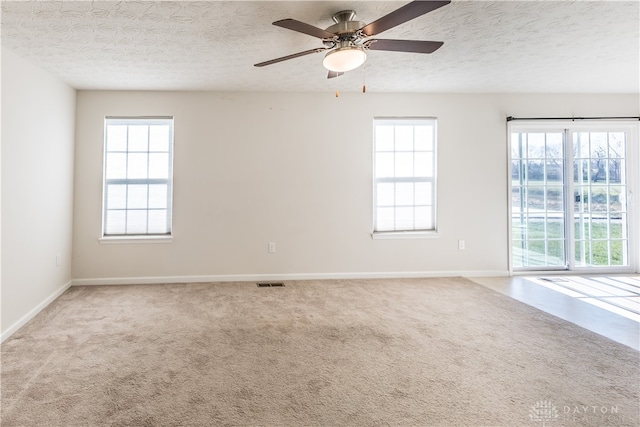 spare room with ceiling fan, plenty of natural light, carpet floors, and a textured ceiling