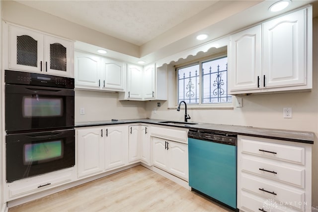 kitchen featuring stainless steel dishwasher, sink, white cabinetry, and black double oven