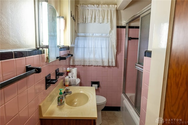 full bathroom with combined bath / shower with glass door, vanity, tile walls, tile patterned flooring, and toilet