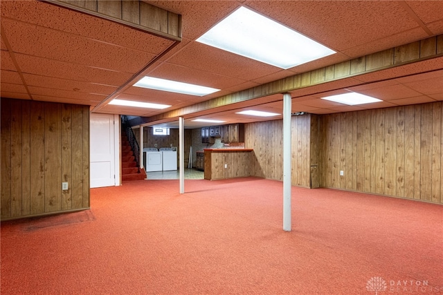 basement with washer and clothes dryer, a drop ceiling, carpet floors, and wooden walls