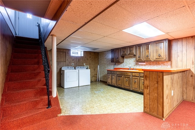 interior space with washer and clothes dryer, a paneled ceiling, sink, and wooden walls