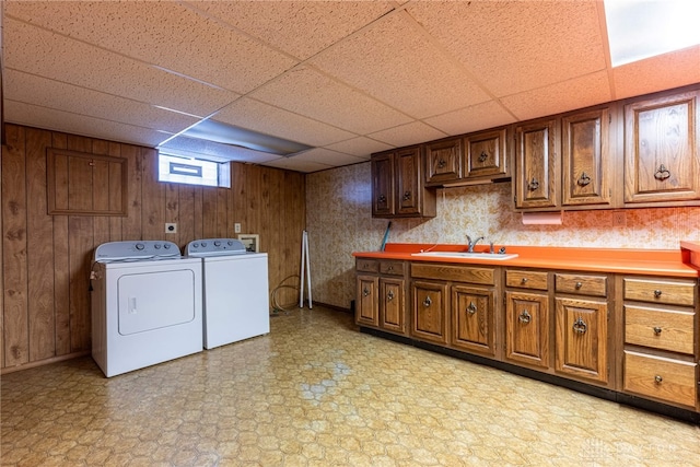 clothes washing area with cabinets, wood walls, washing machine and dryer, and sink