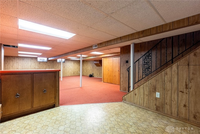 basement featuring a paneled ceiling and wooden walls