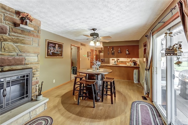 dining area with a fireplace, ceiling fan, a textured ceiling, and light hardwood / wood-style flooring