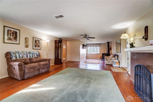 living room with hardwood / wood-style flooring, a wood stove, and ceiling fan