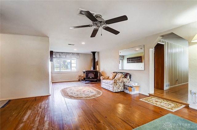 unfurnished room with ceiling fan, wood-type flooring, and a wood stove