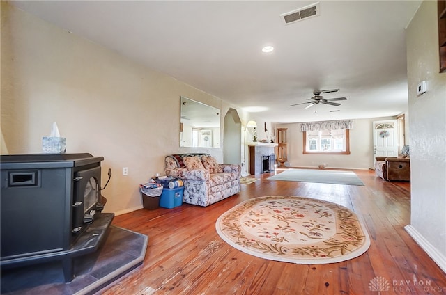 living room featuring ceiling fan, wood-type flooring, and a wood stove