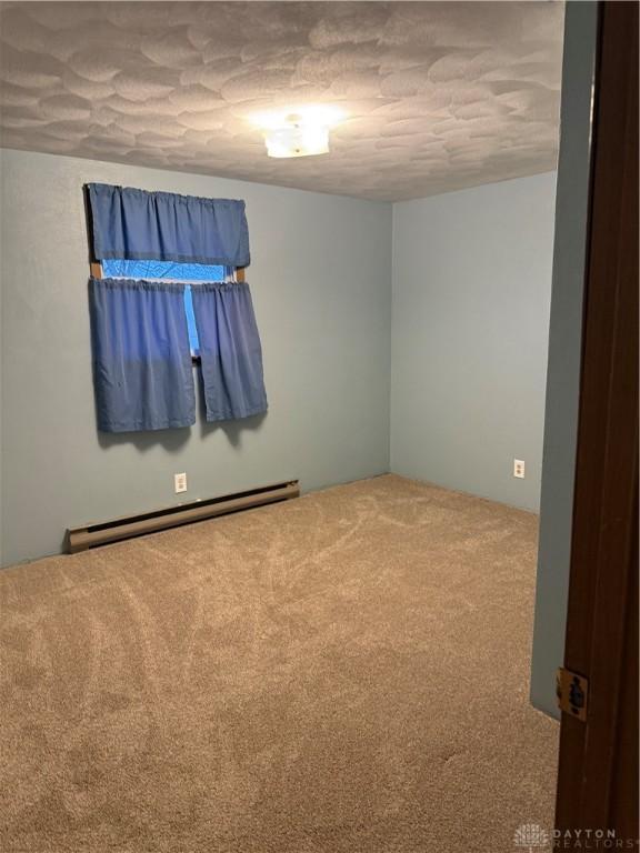 carpeted spare room featuring a textured ceiling and a baseboard heating unit