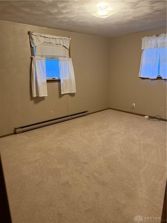 carpeted empty room with a textured ceiling and a baseboard radiator