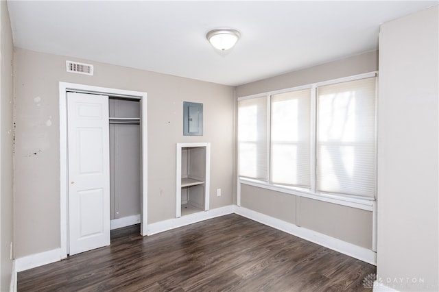 unfurnished bedroom with electric panel, a closet, and dark hardwood / wood-style floors