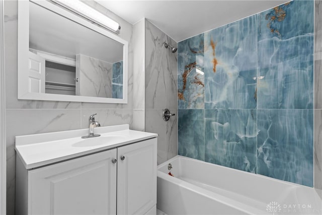 bathroom with vanity, tiled shower / bath combo, tasteful backsplash, and tile walls