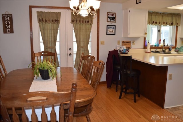 dining space with sink, light hardwood / wood-style floors, and a notable chandelier