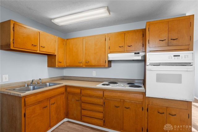 kitchen featuring a textured ceiling, white appliances, light hardwood / wood-style floors, and sink