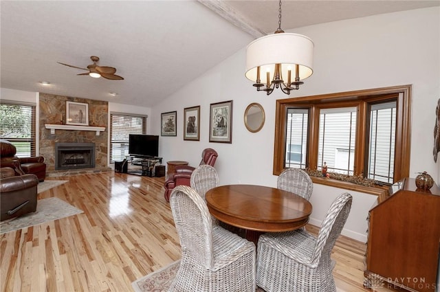 dining space featuring lofted ceiling, a fireplace, light hardwood / wood-style floors, and ceiling fan with notable chandelier