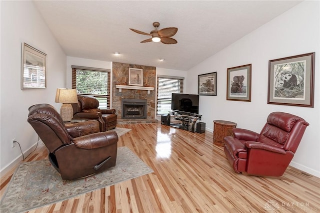 living room featuring ceiling fan, a healthy amount of sunlight, vaulted ceiling, a fireplace, and light wood-type flooring