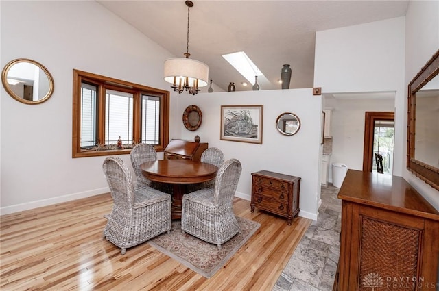 dining room with a chandelier, high vaulted ceiling, a skylight, and light hardwood / wood-style flooring