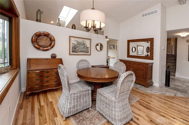 dining space with vaulted ceiling with skylight, a notable chandelier, and light hardwood / wood-style flooring