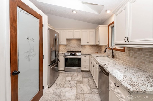 kitchen with lofted ceiling, sink, appliances with stainless steel finishes, light stone counters, and white cabinetry