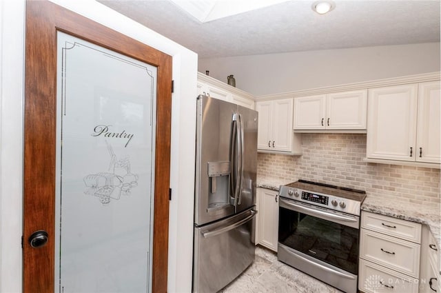 kitchen with white cabinets, vaulted ceiling, light stone countertops, tasteful backsplash, and stainless steel appliances