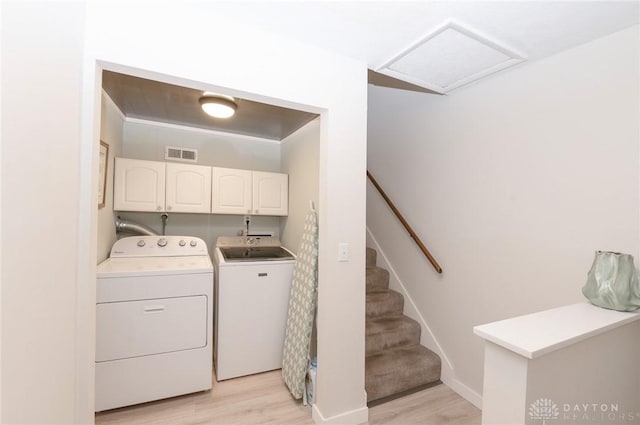 clothes washing area featuring washer and dryer, light hardwood / wood-style floors, and cabinets