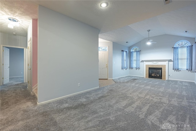 unfurnished living room featuring carpet, lofted ceiling, ceiling fan, a textured ceiling, and a tiled fireplace