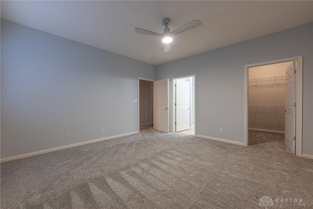 unfurnished bedroom featuring a spacious closet, a closet, ceiling fan, and light carpet