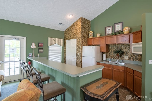 kitchen with sink, a kitchen breakfast bar, lofted ceiling, a textured ceiling, and white appliances