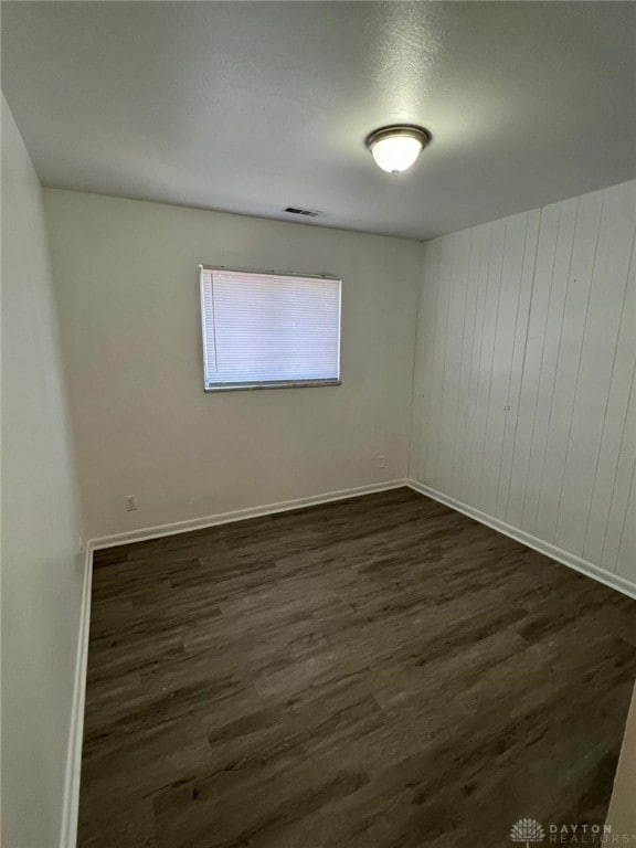 empty room with wooden walls and dark wood-type flooring