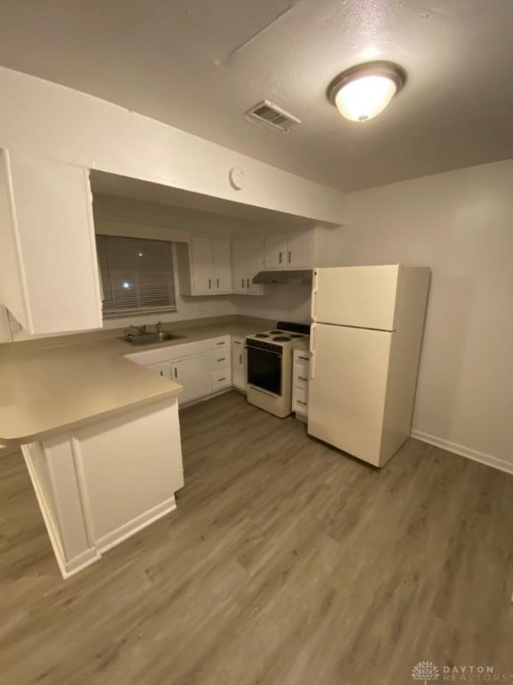 kitchen featuring kitchen peninsula, white appliances, dark wood-type flooring, sink, and white cabinets