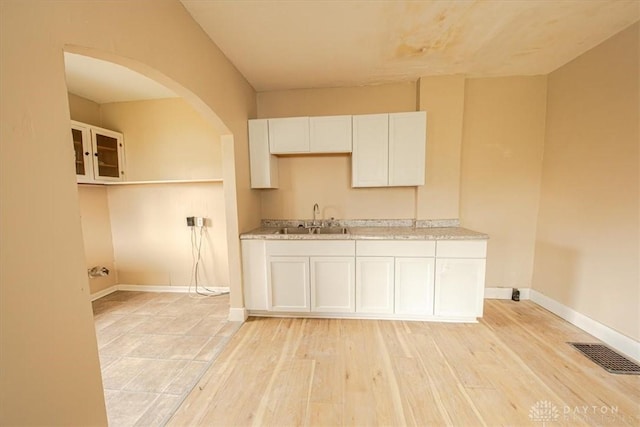 kitchen with white cabinets, light hardwood / wood-style floors, light stone countertops, and sink