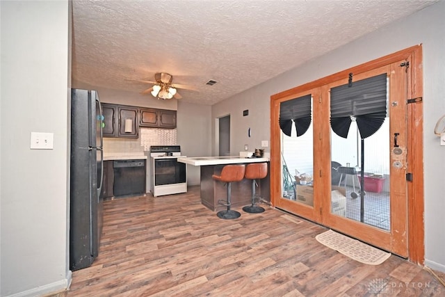 kitchen with a kitchen bar, a textured ceiling, hardwood / wood-style flooring, and black appliances