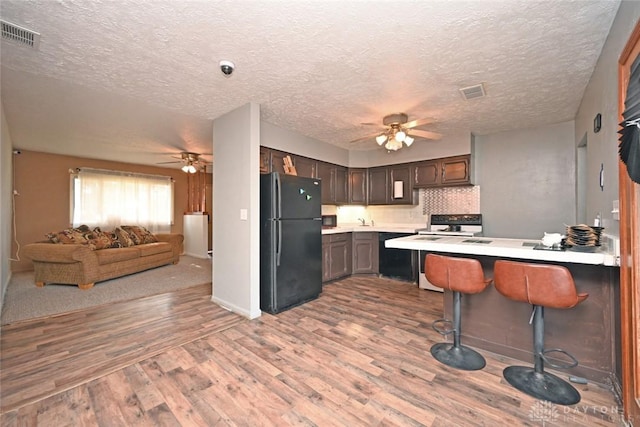 kitchen featuring black appliances, a kitchen breakfast bar, kitchen peninsula, a textured ceiling, and wood-type flooring