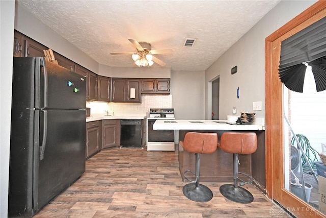 kitchen featuring kitchen peninsula, a textured ceiling, black appliances, light hardwood / wood-style flooring, and a breakfast bar area