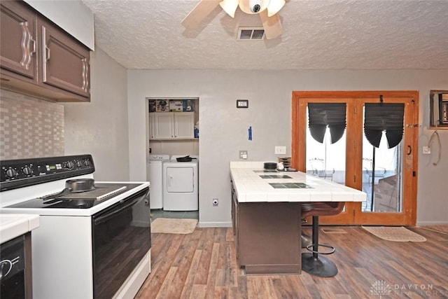 kitchen with light hardwood / wood-style flooring, electric range, separate washer and dryer, a textured ceiling, and a breakfast bar area