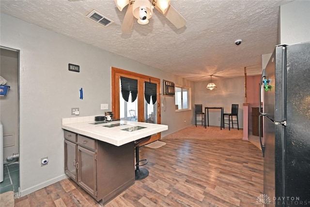 kitchen with kitchen peninsula, black fridge, decorative light fixtures, hardwood / wood-style flooring, and tile counters