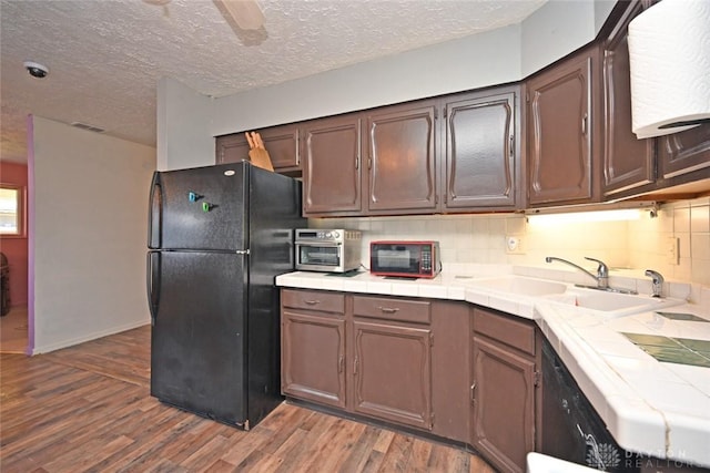 kitchen featuring decorative backsplash, black fridge, sink, tile countertops, and dark hardwood / wood-style floors