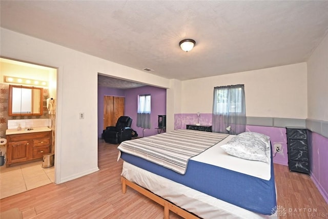 bedroom with a textured ceiling, ensuite bath, light hardwood / wood-style floors, and multiple windows