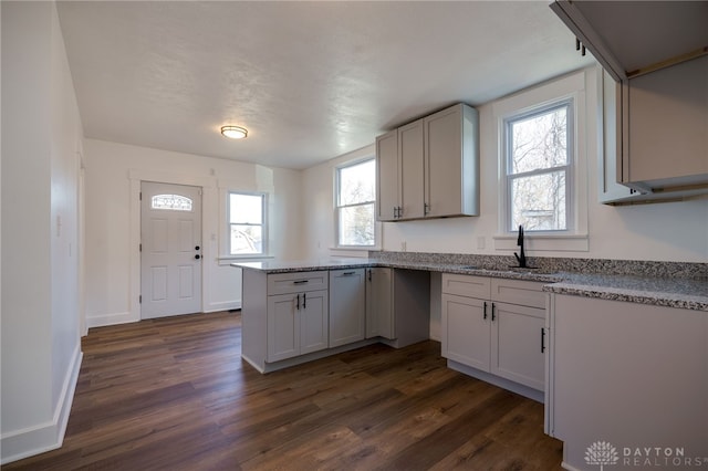 kitchen featuring light stone countertops, white cabinetry, sink, dark wood-type flooring, and kitchen peninsula