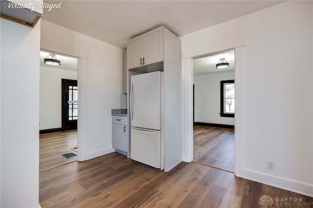 kitchen with white cabinetry, dark hardwood / wood-style flooring, light stone counters, and white refrigerator