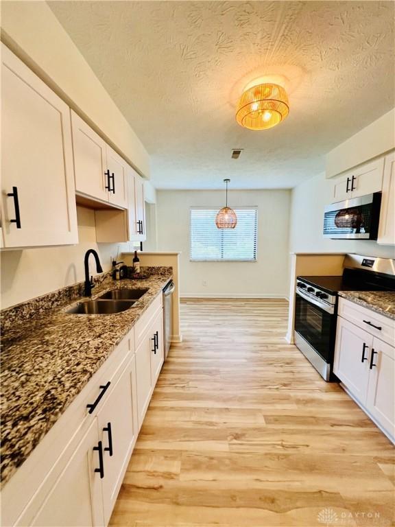 kitchen featuring pendant lighting, sink, light hardwood / wood-style floors, white cabinetry, and stainless steel appliances