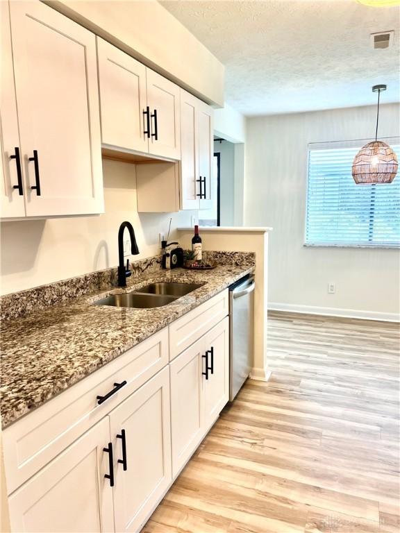 kitchen featuring pendant lighting, dishwasher, stone counters, sink, and light hardwood / wood-style floors