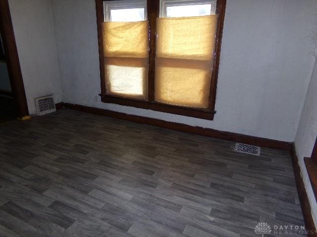 spare room with dark wood-style floors, visible vents, and baseboards