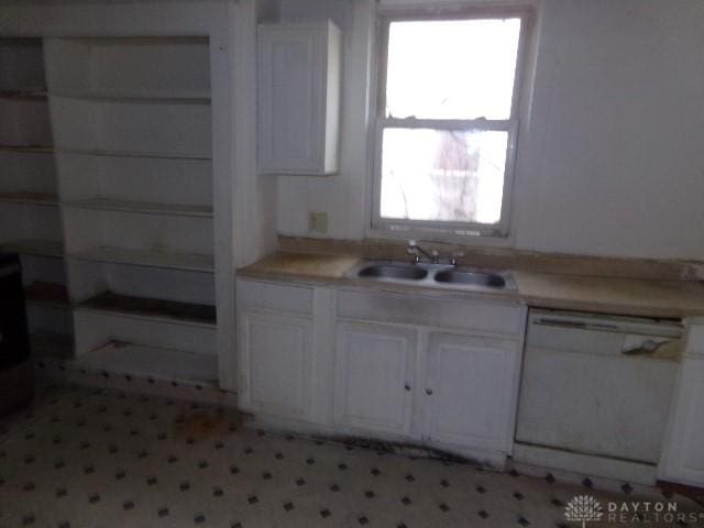 kitchen with white dishwasher, white cabinetry, light countertops, and a sink