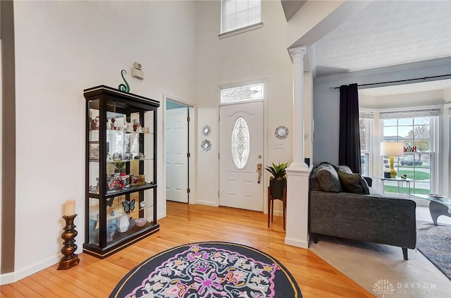 foyer entrance with light wood-type flooring, decorative columns, and crown molding