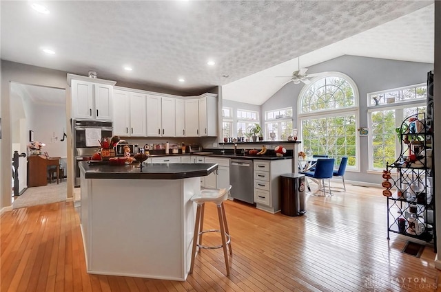 kitchen with vaulted ceiling, ceiling fan, light wood-type flooring, appliances with stainless steel finishes, and white cabinetry