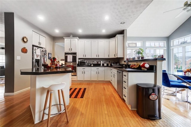 kitchen featuring a breakfast bar, white cabinets, vaulted ceiling, light wood-type flooring, and stainless steel appliances