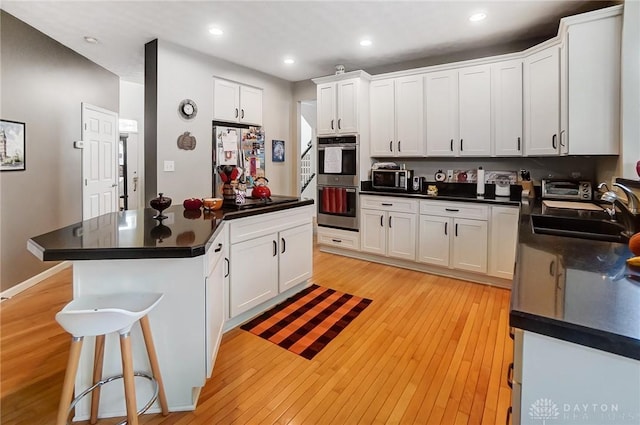 kitchen featuring stainless steel appliances, sink, light hardwood / wood-style flooring, a center island, and white cabinetry