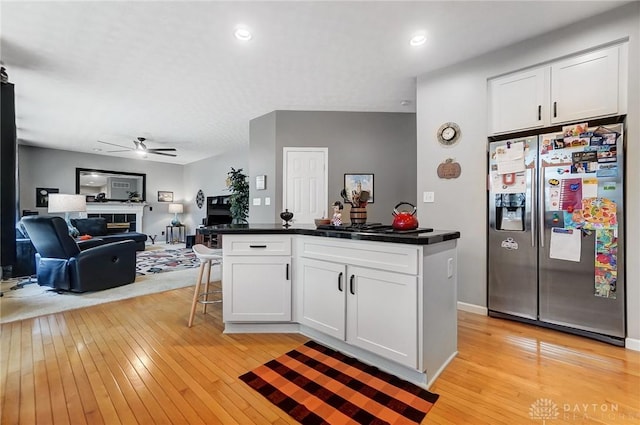 kitchen with a tile fireplace, stainless steel refrigerator with ice dispenser, ceiling fan, light hardwood / wood-style floors, and white cabinetry