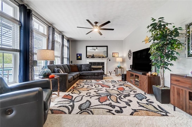 living room with a tile fireplace, light colored carpet, and ceiling fan